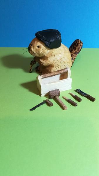 Une sculpture de castor avec une caisse à outils. Il y a une scie, une lime, un manteau et deux tournevis