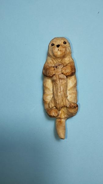 Une sculpture de loutre en bois. Elle est allongée sur le dos et enlace son petit