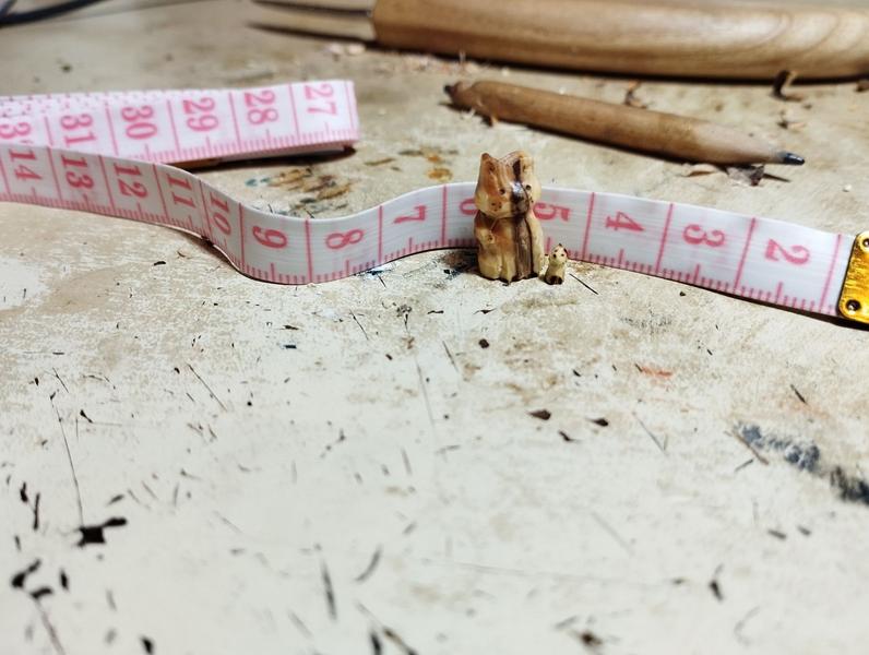 deux sculptures en bois : un chat et tout petit renardelles sont devant un mètre ruban. Le grand chat mesure 2cm de haut, le renard environ 5 mm