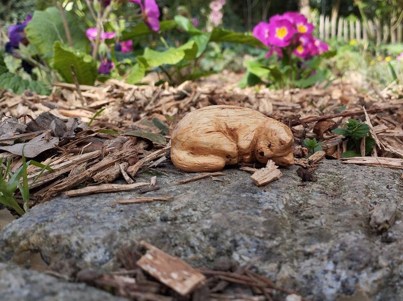 Photo d'une sculpture de chat. Le chat dort sur une pierre. En fond, des primevères violettes