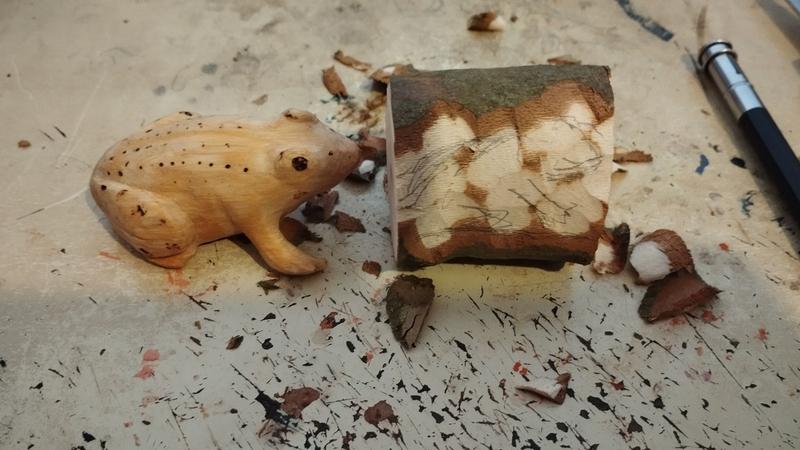Une sculpture de grenouille en bois à côté d'un morceau de bois. Dessus est dessiné une esquisse de grenouille