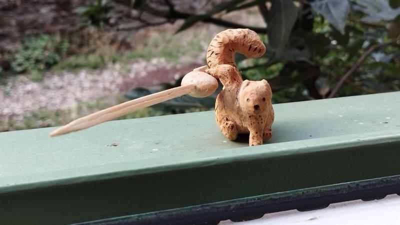 Un petit écureuil en bois 3n position atterrissage de super-héros : un point au sol, l'autre tient une épée