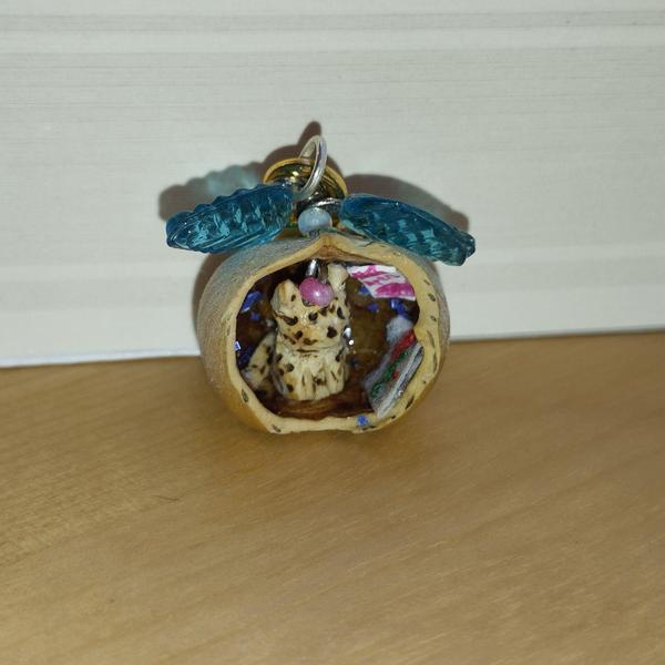 Un pendentif noisette avec un chat tigré à l'intérieur. Au dessus, deux feuilles bleues transparentes