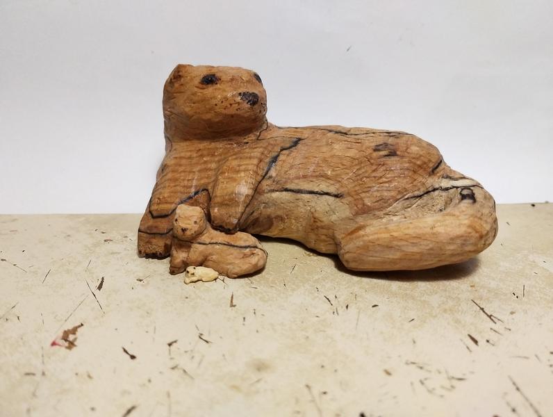 Trois sculptures de loutres allongées.Elles prennent la même pose mais sont de tailles différentes. La moyenne est sous la patte de la plus grande, et la mini sous la patte de la moyenne 