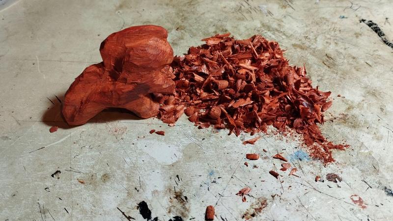 Une sorte de dinosaure bipède en bois pas fini à côté d'un tas de copeaux