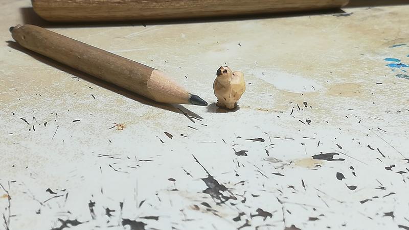 Mini sculpture d'un poussin à côté d'un crayon. Le poussin est un peu plus haut que le crayon 
