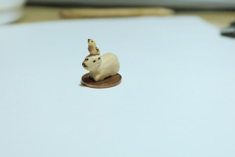 Mini sculpture en bois de capybara posée sur une pièce d'un centime. Il y a un oiseau sur sa tête 