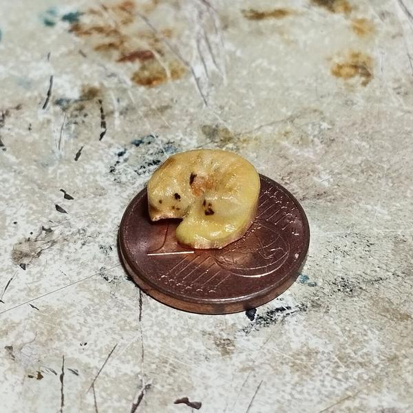 Un mini chat en bois qui dort en boule. La sculpture est posée sur une pièce d'un centime