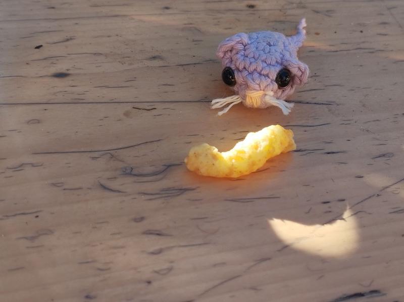 Une petite souris au crochet. Elle regarde un gâteau apéritif. L'ensemble est à l'ombre mais la lumière resplendit sur le gâteau