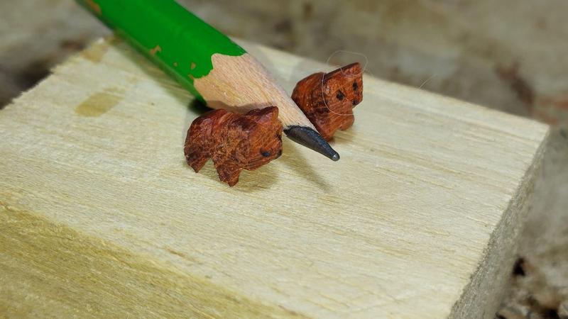 Deux petites sculptures en bois. Elles font penser à des petits chiens ou des oursons. Elles encadrent un crayon gris posé à plat. Elles ne sont pas beaucoup plus hautes que le crayon
