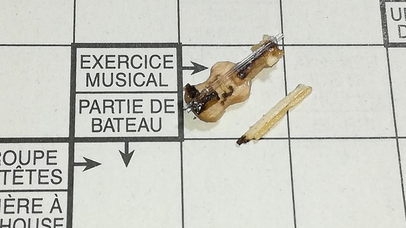 Gros plan sur le mini violon en bois posé sur une case de mots fléchés à côté de la définition "exercice musical" 