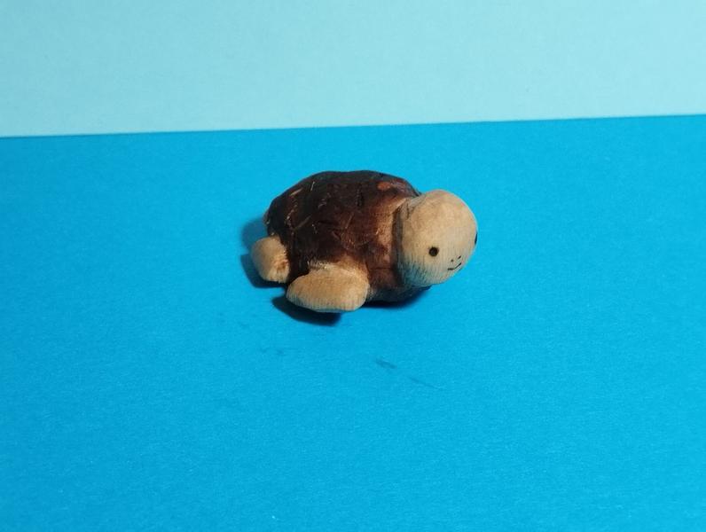 Une sculpture de tortue en bois, la carapace est plus foncée que le corps