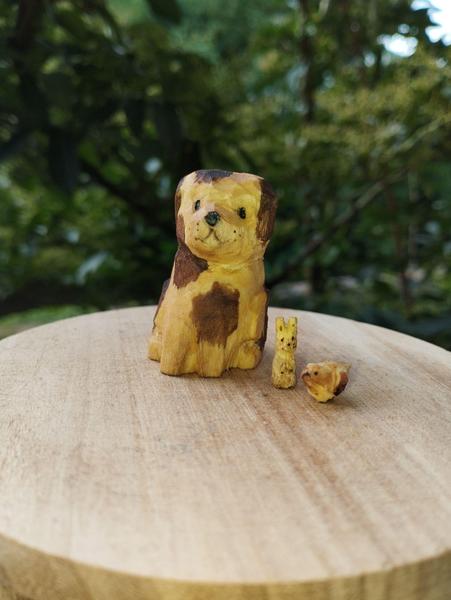 Trois sculptures en bois : un chien, beige et marron, oreilles collées, un mini lapin et un mini oiseau