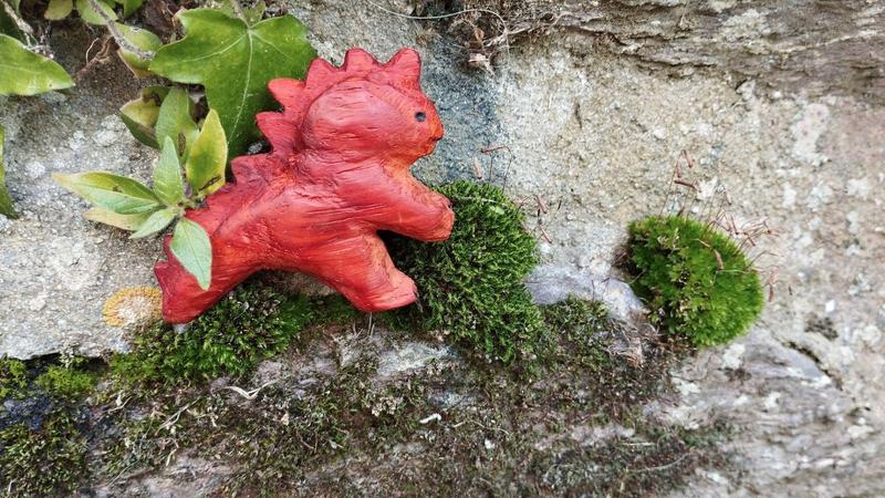 Un dinosaure bipède en bois rouge sur  la façade d'un muret, à côté d'une boule de mousse