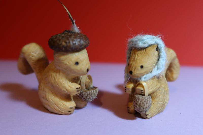 two sculptures of squirrels.They both hold a basket, one wear a feathered hat, the other a cap