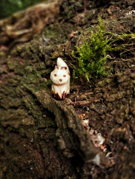 Un petit renard en bois sur un tronc à côté d'un buisson de mousse