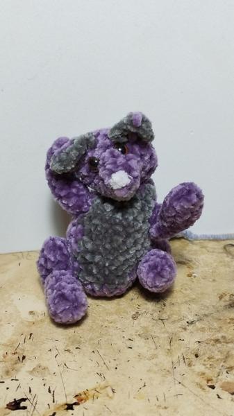 Un rat violet et gris au crochet. Il est assis et se gratte l'oreille 