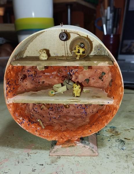 Une scène miniature dans une boîte rondeIl y a trois étages. Le plus haut est agrémenté d'une grue à roue qui sert à descendre un panier. Dans la roue, il y a un hamster. Les parois des deux étages inférieurs font penser à une mine. Un renard et sa brouette se trouve à l'étage du milieu. 