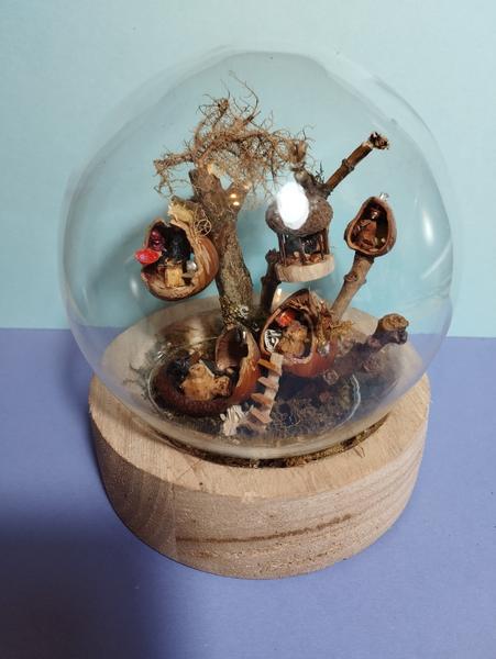 Un arbre avec des cabanes noisettes des mini animaux.L'ensemble est protégé par un globe en verre 