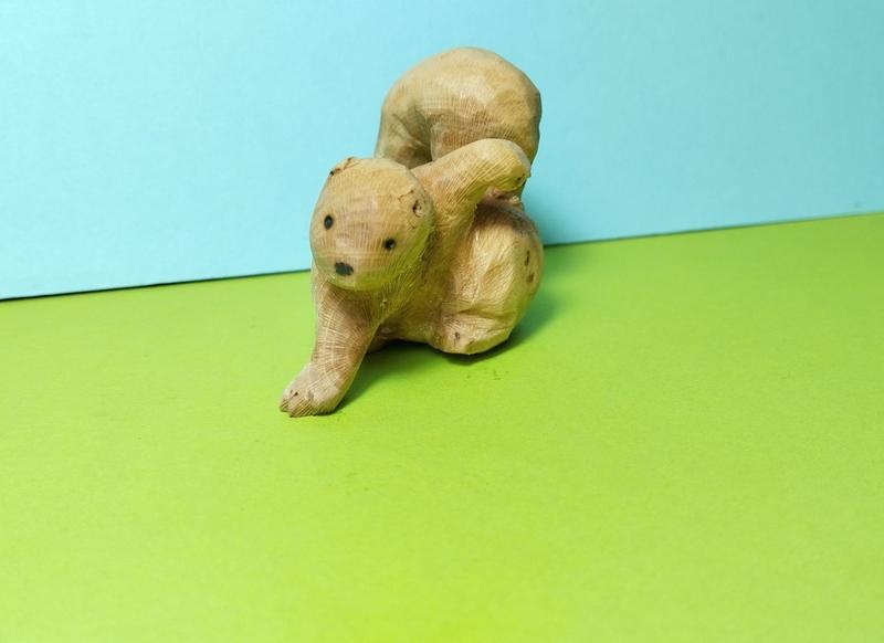 Photo d'une sculpture d'écureuil en bois. Il est en position atterrissage de super héros : une main sur le sol, l'autre bras levé
