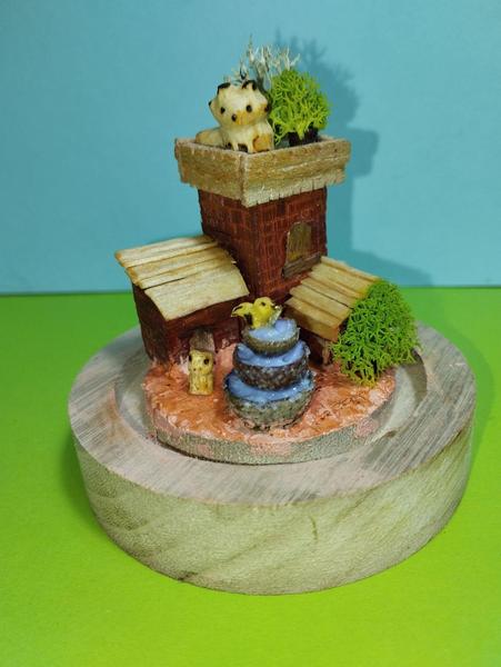 Une scène miniature : une tour et deux annexes. Un renard se trouve sur le toit une fontaine orne la cour. Un oiseau s'y abreuve et une grenouille est assise à côté
