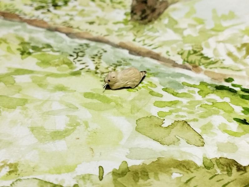 un mini ragondin en bois, posé sur une aquarelle représentant un ruisseau