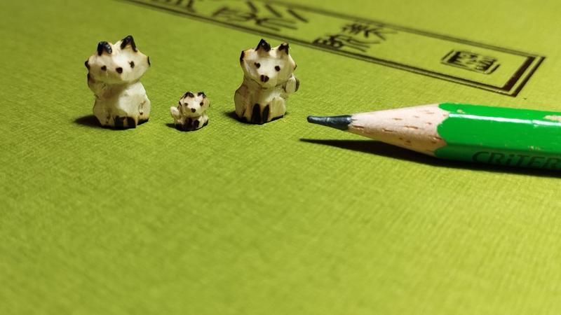 Trois mini sculptures de renard en bois. Celui du milieu est tout petit. À côté, un crayon gris est posé à plat . Le plus petit est à peine plus haut que la mine