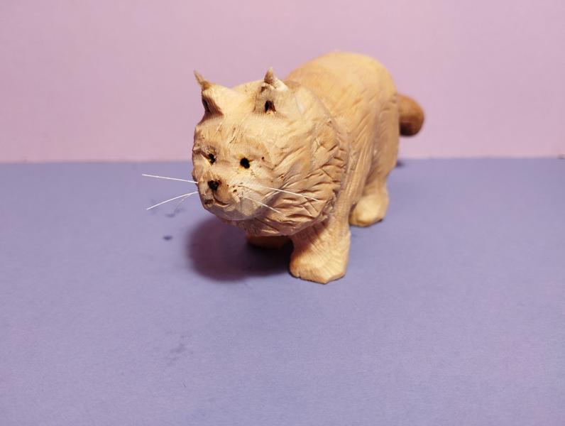 sculpture d'un chat, ressemblant à un main coonil a des longues moustaches blanchesil semble regarder vers un point au sol derrière l'objectif, prêt à foncer (gentiment) sur sa proie