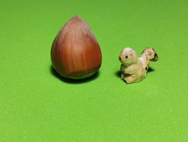 Un petit écureuil en bois à côté d'une noisette. L'écureuil est deux fois moins grand que la noisette 