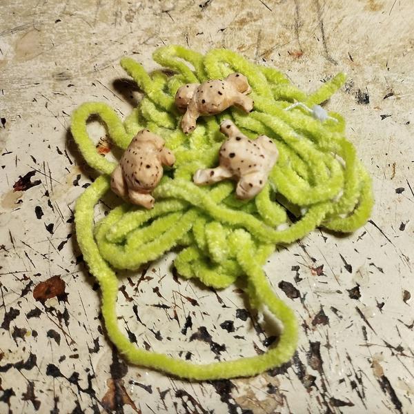 Trois mini grenouilles en bois sur de la laine verte 