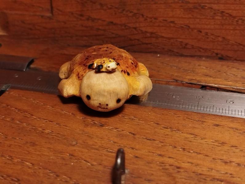 Deux tortues en bois, dont une mini. La mini est sur la tête de la plus grande. Les carapaces sont oranges