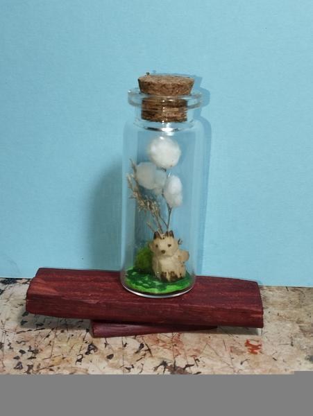 Photo d'une fiole en verre. À l'intérieur, un petit renard en bois qui veille sur son jardin