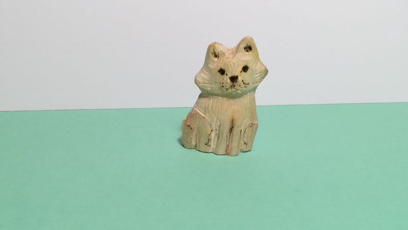 Sculpture de chat en bois. Le chat est assis et penche légèrement sa tête sur le côté 