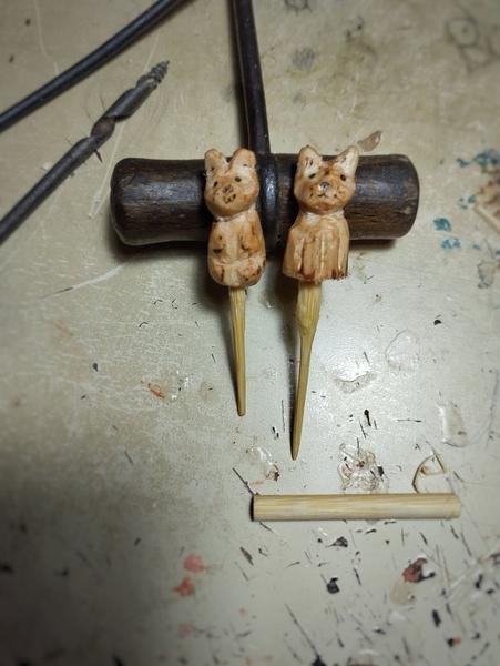 Deux épingles en bambou décorées avec des embouts sculptures d'animaux. À côté in morceau de baguette en bambou 