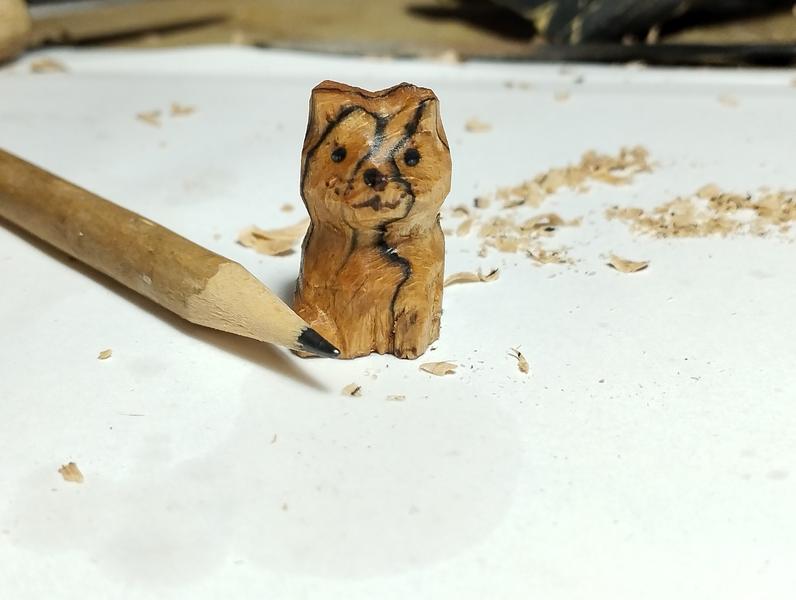 Une petite sculpture de chat en bois. Des marbrures traversent son corps et sa tête 