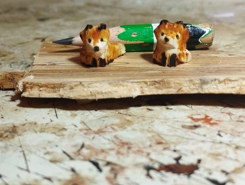 Deux petits renards en bous teints en orange. Derrière eux, un crayon gris proche de la fin. Les renards sont un peu plus grands que la largeur du crayon