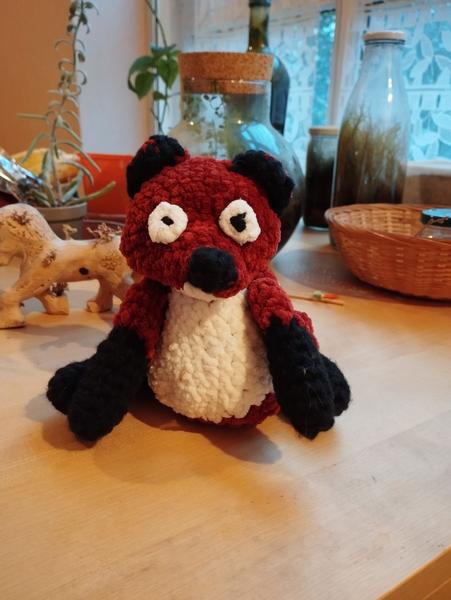 Un renard au crochet, rouge foncé, blanc et noir. Il a une texture fluffy 
