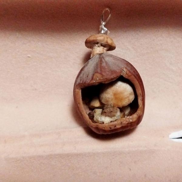 Pendentif noisette. Dedans, il y a des champignons et un chat qui dort 