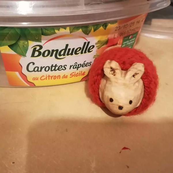 Sculpture de lapin dans un sac de couchage crocheté. Vue de face. Derrière il y a une boîte de carottes râpées
