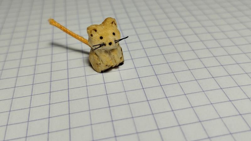 Un petit rongeur en bois. Il a des moustaches noire en nylon et une queue orange en cordon