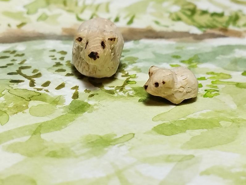 Deux moutons en bois posés sur une aquarelle verte. L'un des moutons est tout petit 