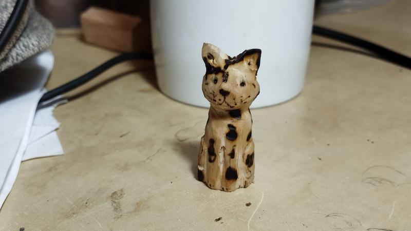 Une sculpture de chat en bois, à côté avec des tâches pyrogravées