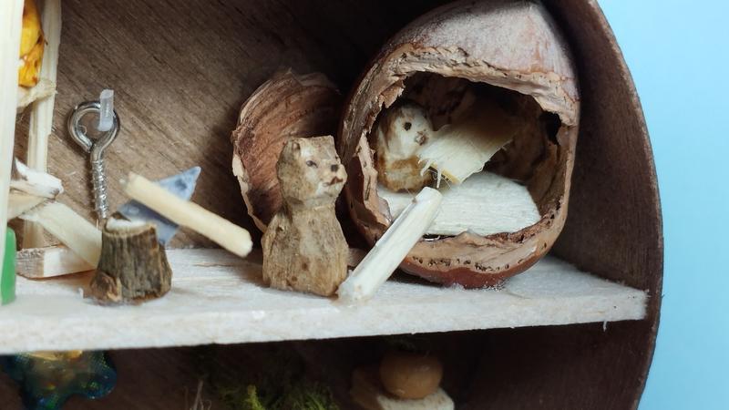 Gros plan sur une noisette. Un chat passe une planche a un oiseau. Celui-ci est dans la noisette et pose une autre planche avec son becUne hache est plantée dans une souche d'arbre