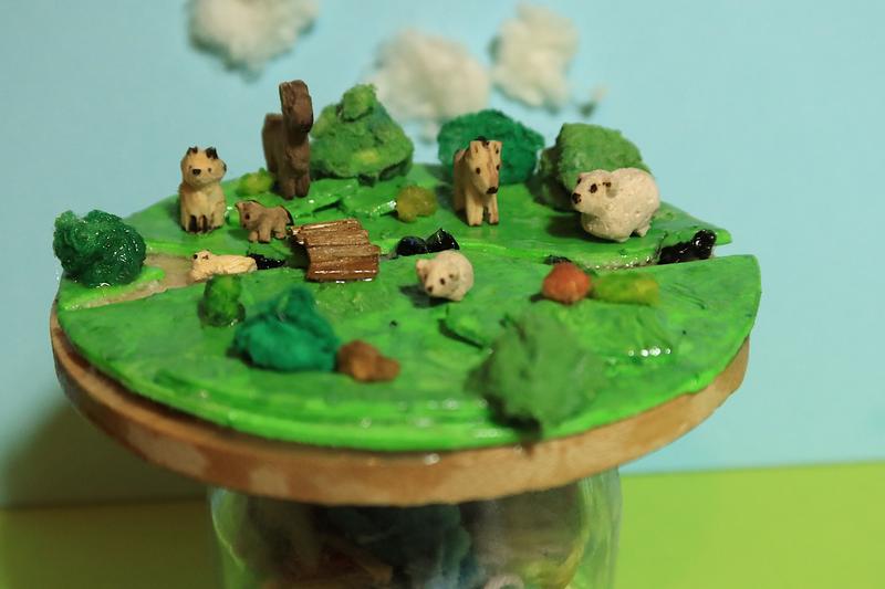 Une petite prairie sur un rond de bois. Il y a plusieurs animaux, un renard, un alpaga, deux poneys, un mouton et une loutre.