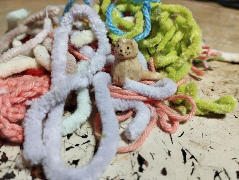 Un petit chat en bois au milieu d'un amas de fils de différentes tailles et couleurs