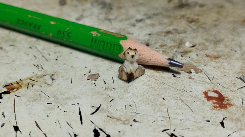 Un mini renard en bois devant un crayon posé à plat. Le renard est à peine plus grand que le crayon