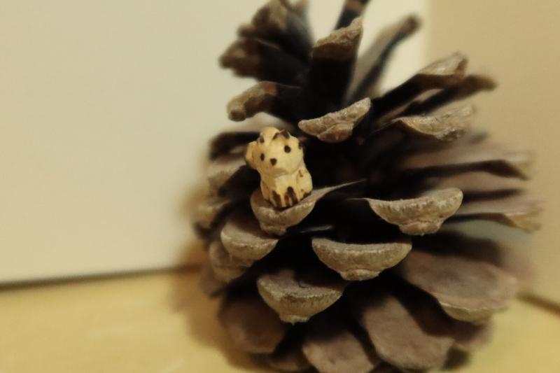 Photo d'un mini kitsune en bois posé sur un pignon de pomme de pin 