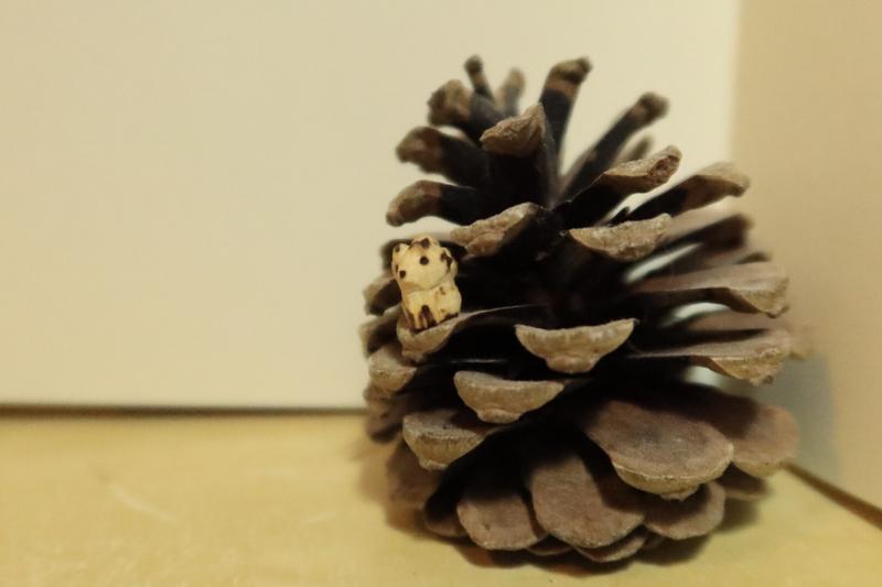 Photo d'un mini kitsune en bois posé sur un pignon de pomme de pin 