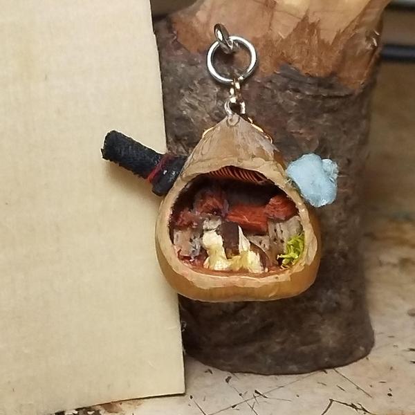 Photo d'un pendentif noisetteCollés a l'extérieur : un haut de forme noir et une casquette bleueDans la noisette : un basset et un village en arrière-plan