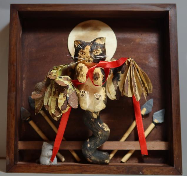 Sculpture de Sarabi, avec des ailesSarabi montre son ventre qu'on veut caresserElle tient un ruban rouge dont l'une des extrémité est tenue par un petit chat grisEn arrière plan, il y a 4 lances et la lune